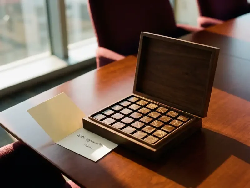 Luxe geschenkdoos met gepersonaliseerde Belgische chocolaatjes op mahonie vergadertafel met handgeschreven bedankbrief