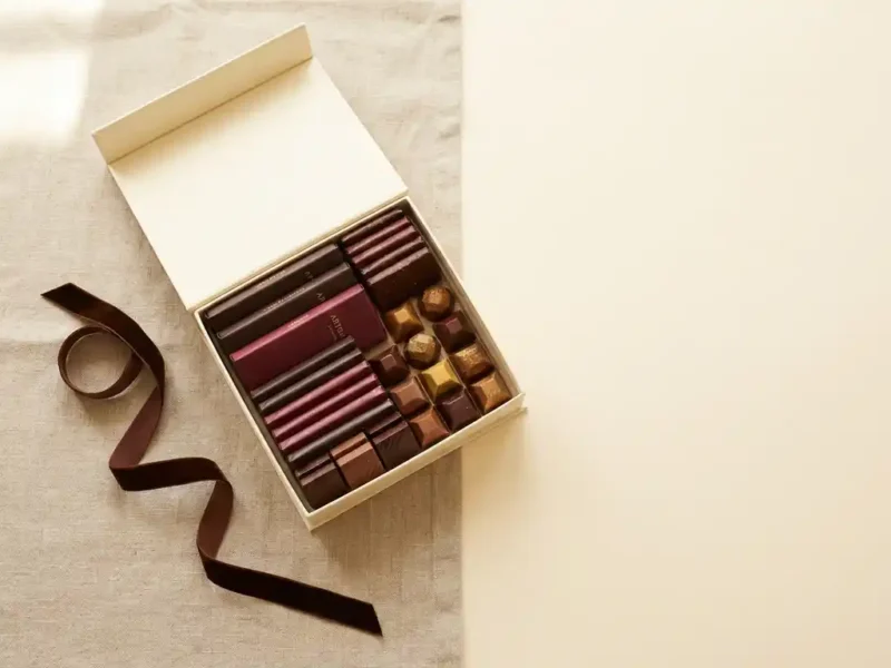 Elegante geschenkdoos gevuld met ambachtelijke chocoladerepen en pralines op linnen, met donker lint en warme bruintinten.
